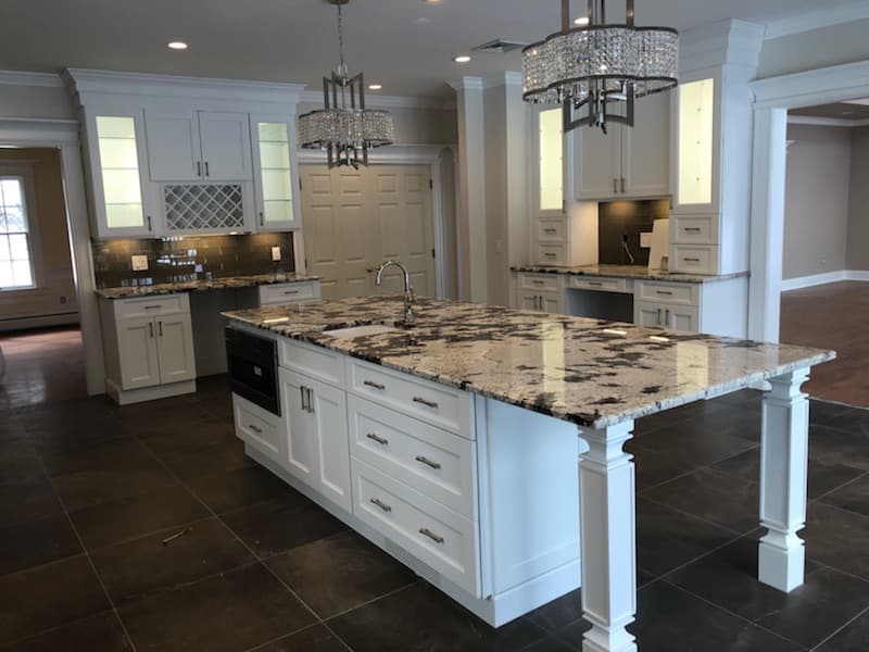 Granite island with pendant chandeliers and glass front upper cabinets