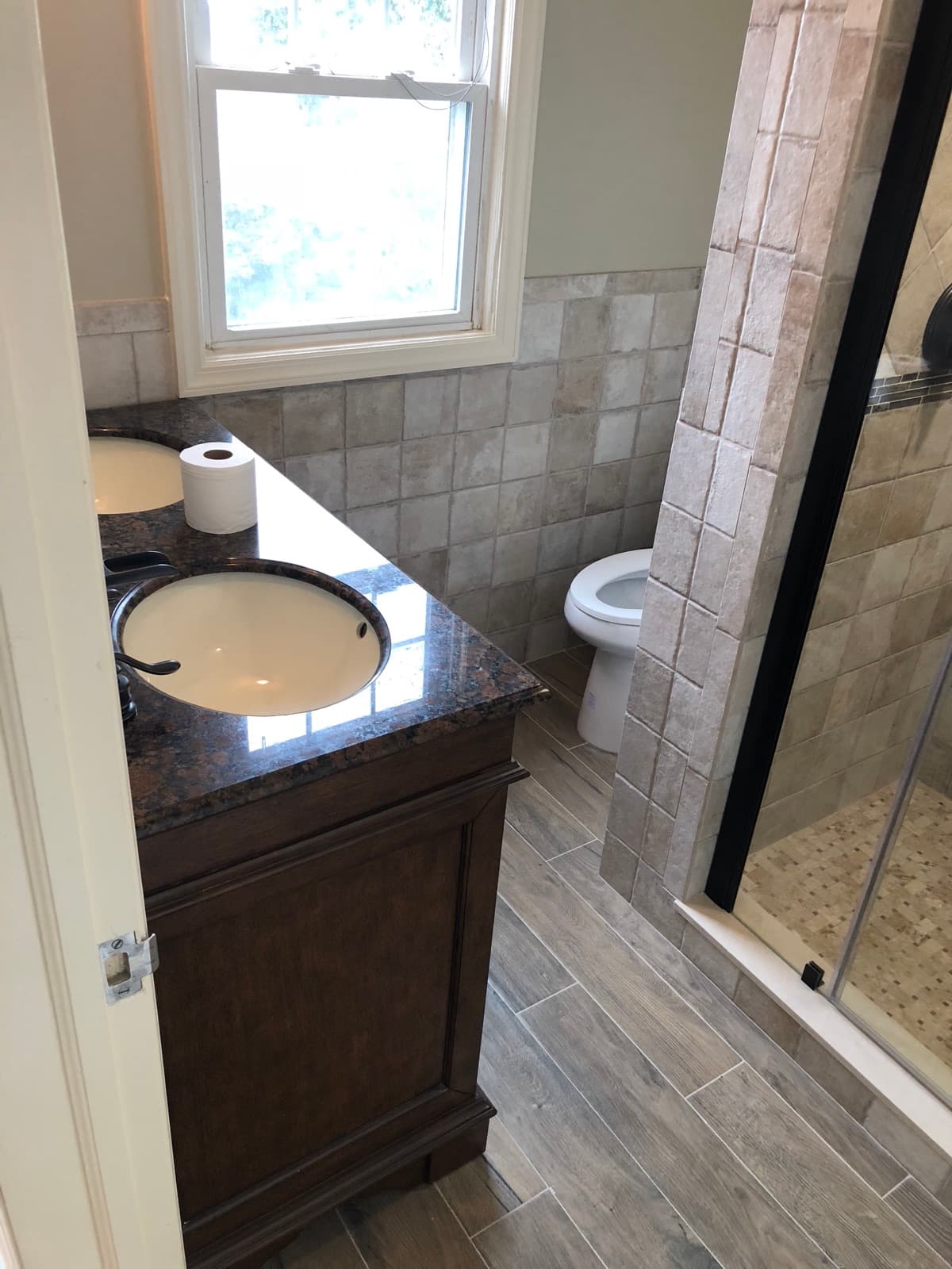 Finished bathroom with a stone topped vanity, tile wainscot and a glass door shower