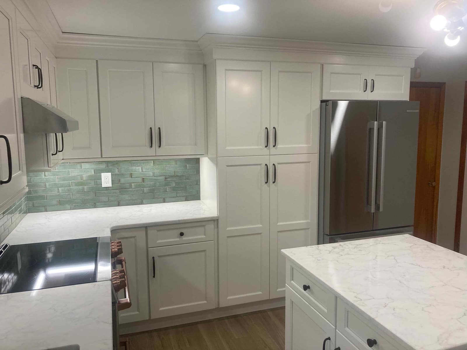 Floor to ceiling pantry cabinets beside a stainless refrigerator in the finished kitchen