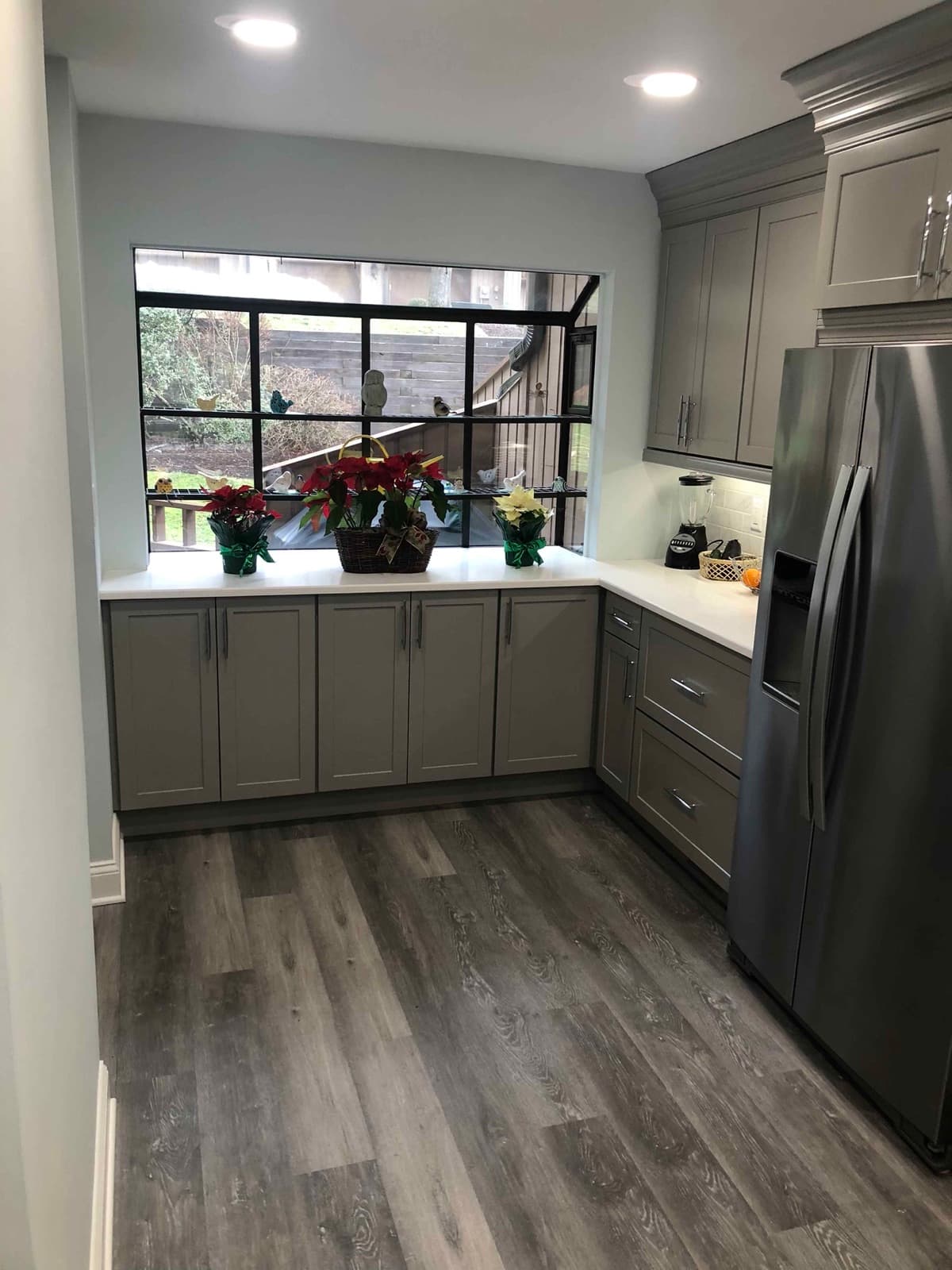 Window run over the kitchen sink with grey cabinets and plank flooring
